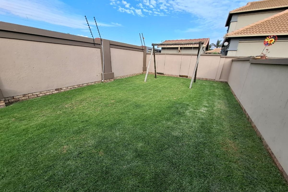 A private rear garden featuring a well-defined lawn area enclosed by high perimeter boundary walls with integrated electric fencing.