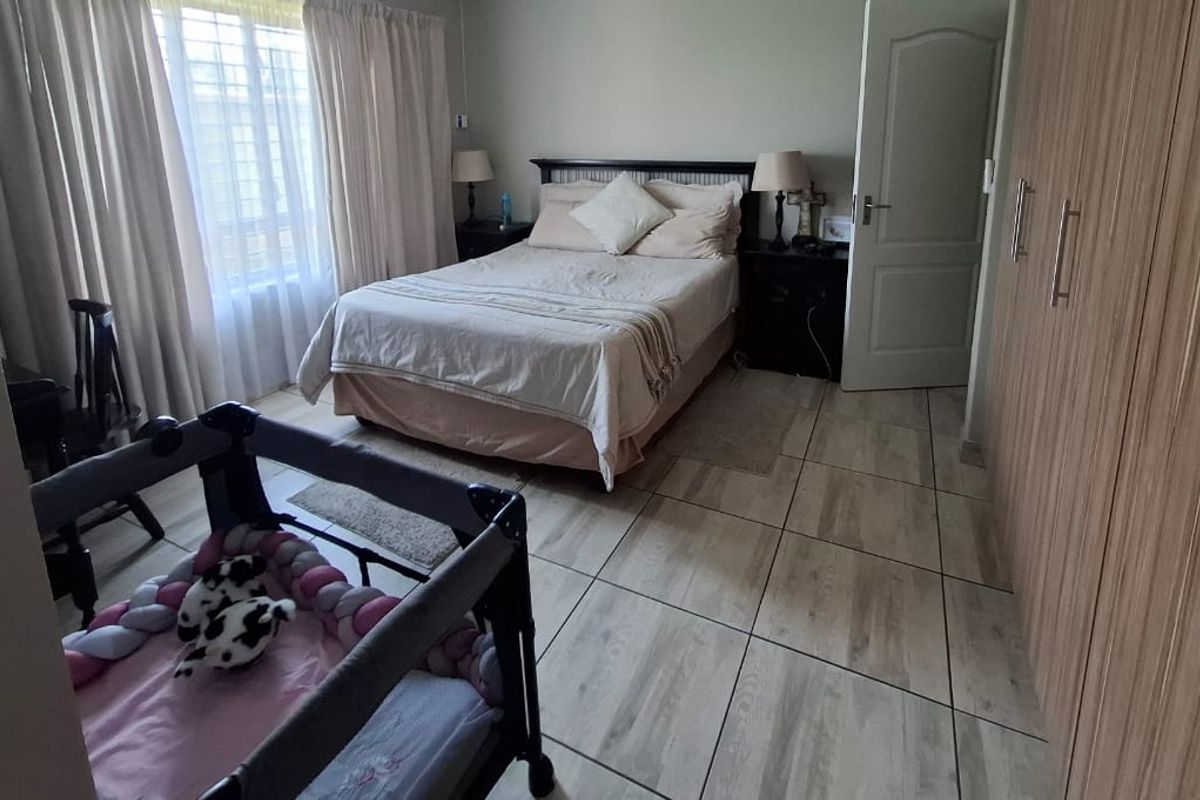 A well-maintained bedroom featuring built-in wooden cupboards, tiled flooring, and large windows with curtains.