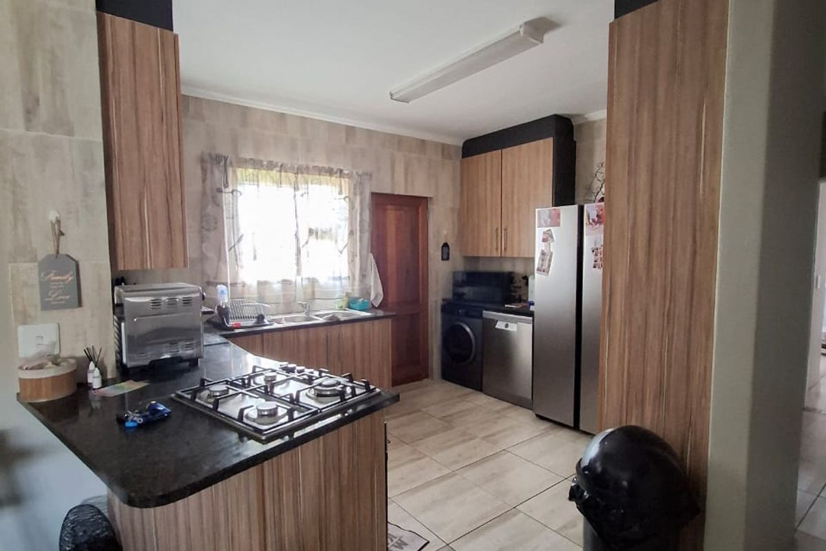 A functional kitchen featuring wood-look cabinetry, dark stone countertops, a built-in gas hob, and tiled flooring throughout.
