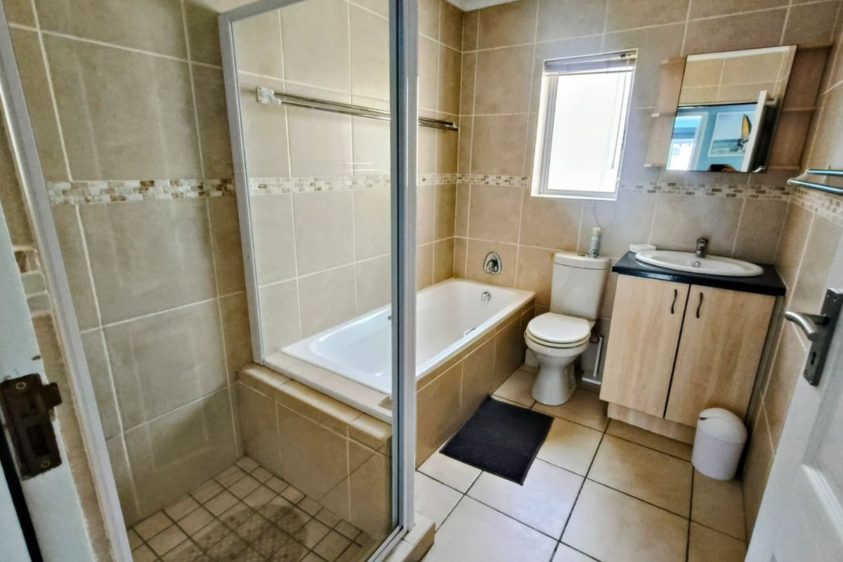 A functional bathroom featuring a separate shower enclosure, a built-in bathtub, a vanity cabinet with a basin, and neutral wall and floor tiling.