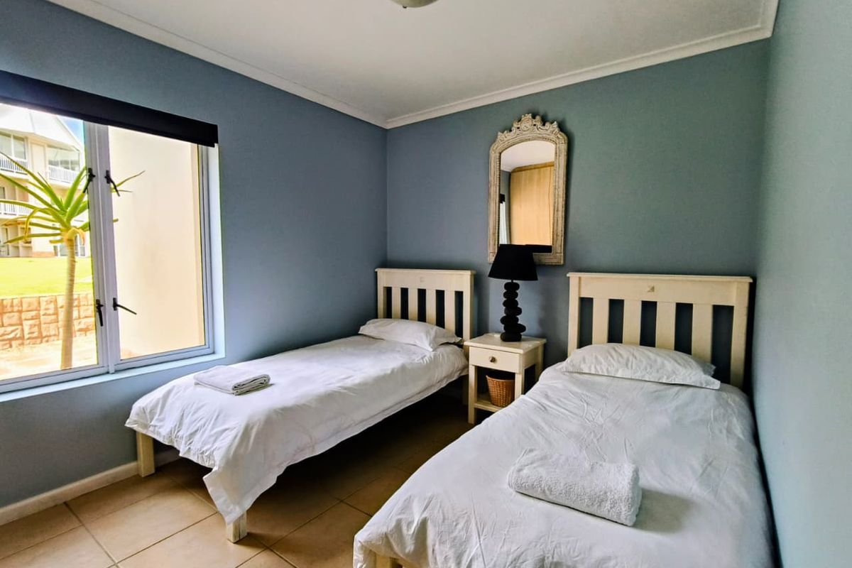 A functional bedroom featuring tiled flooring, blue painted walls, and a large window providing natural light and exterior views.
