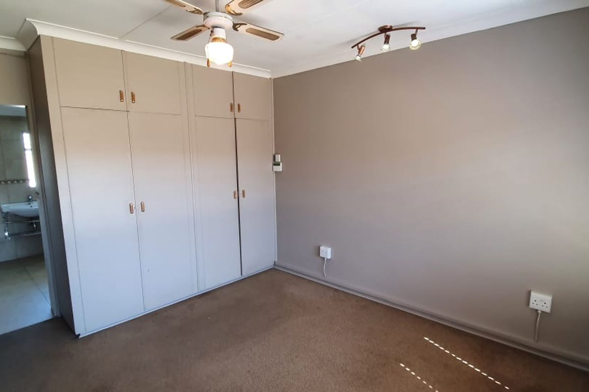 A bedroom featuring built-in cupboards, a ceiling fan, and an adjoining en-suite bathroom with tiled finishes.