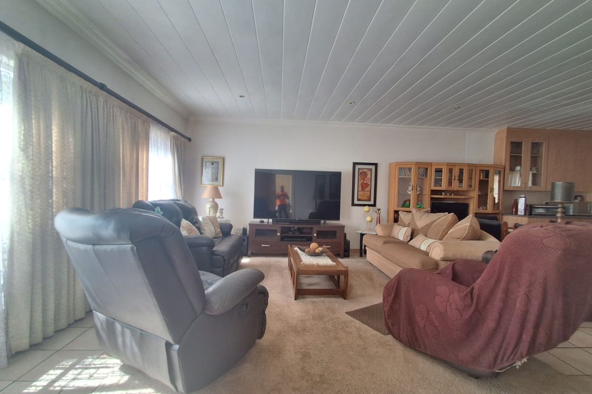 A spacious living area featuring tiled and carpeted flooring, a unique panelled ceiling, and integrated cabinetry, offering a comfortable and functional layout.