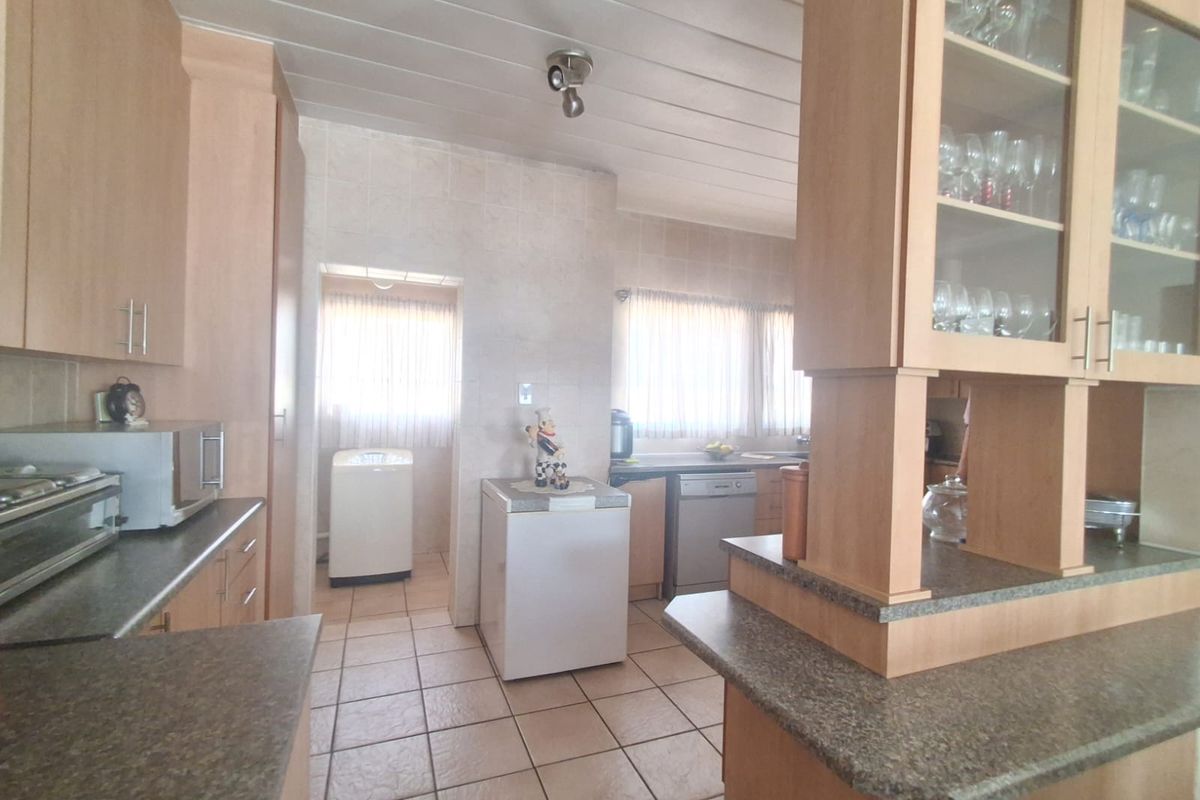 A functional kitchen featuring light wood cabinetry, granite-look countertops, tiled flooring, and a separate scullery area with laundry connections.