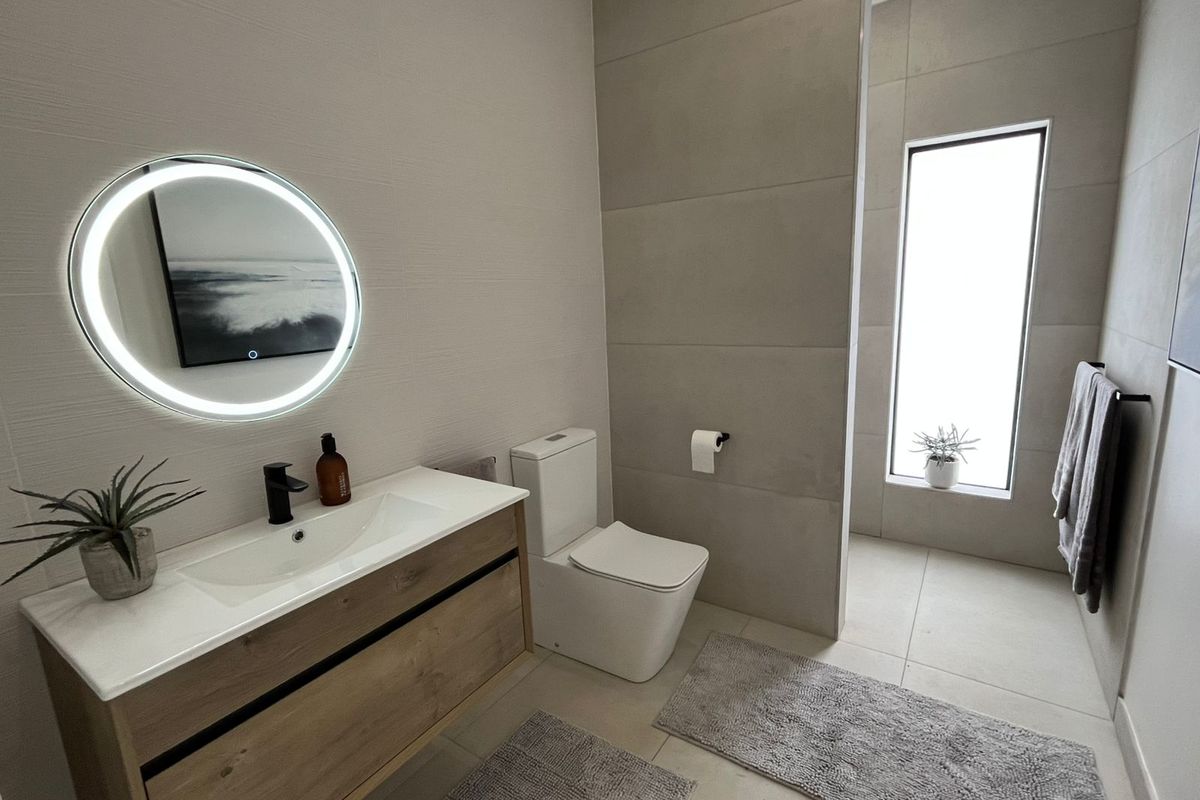 Modern bathroom featuring a floating timber vanity, integrated basin, matte black tapware, LED backlit circular mirror, and large format floor-to-ceiling wall tiles.