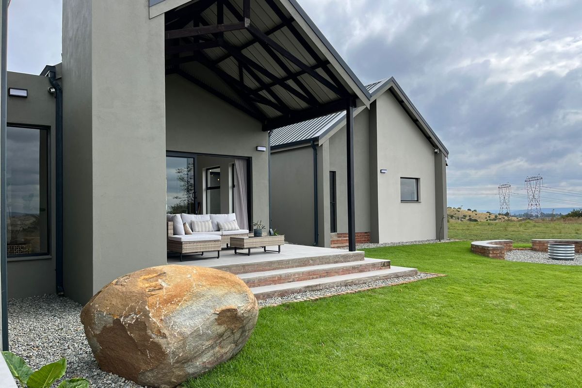 Modern exterior rear view featuring a covered patio with exposed timber trusses, brick steps, and a landscaped garden with a fire pit area.