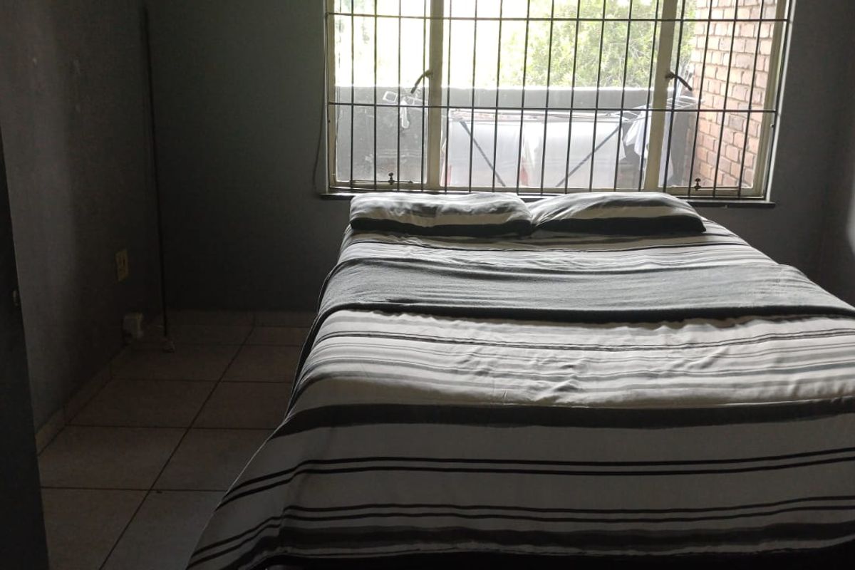 A compact bedroom featuring tiled flooring and a window fitted with security bars, offering a functional space for rest.