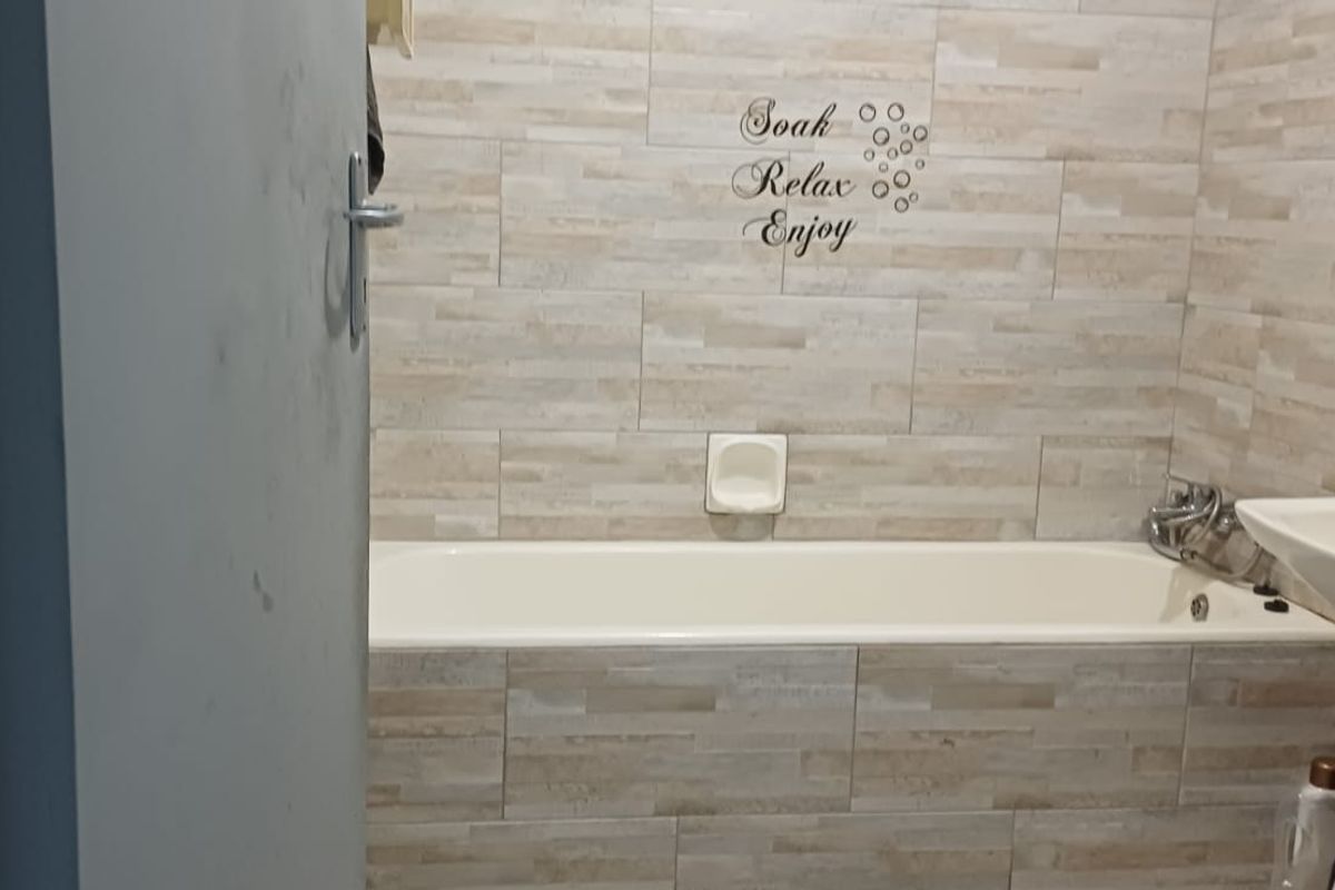A functional bathroom featuring a built-in bathtub with tiled surround and a pedestal washbasin.