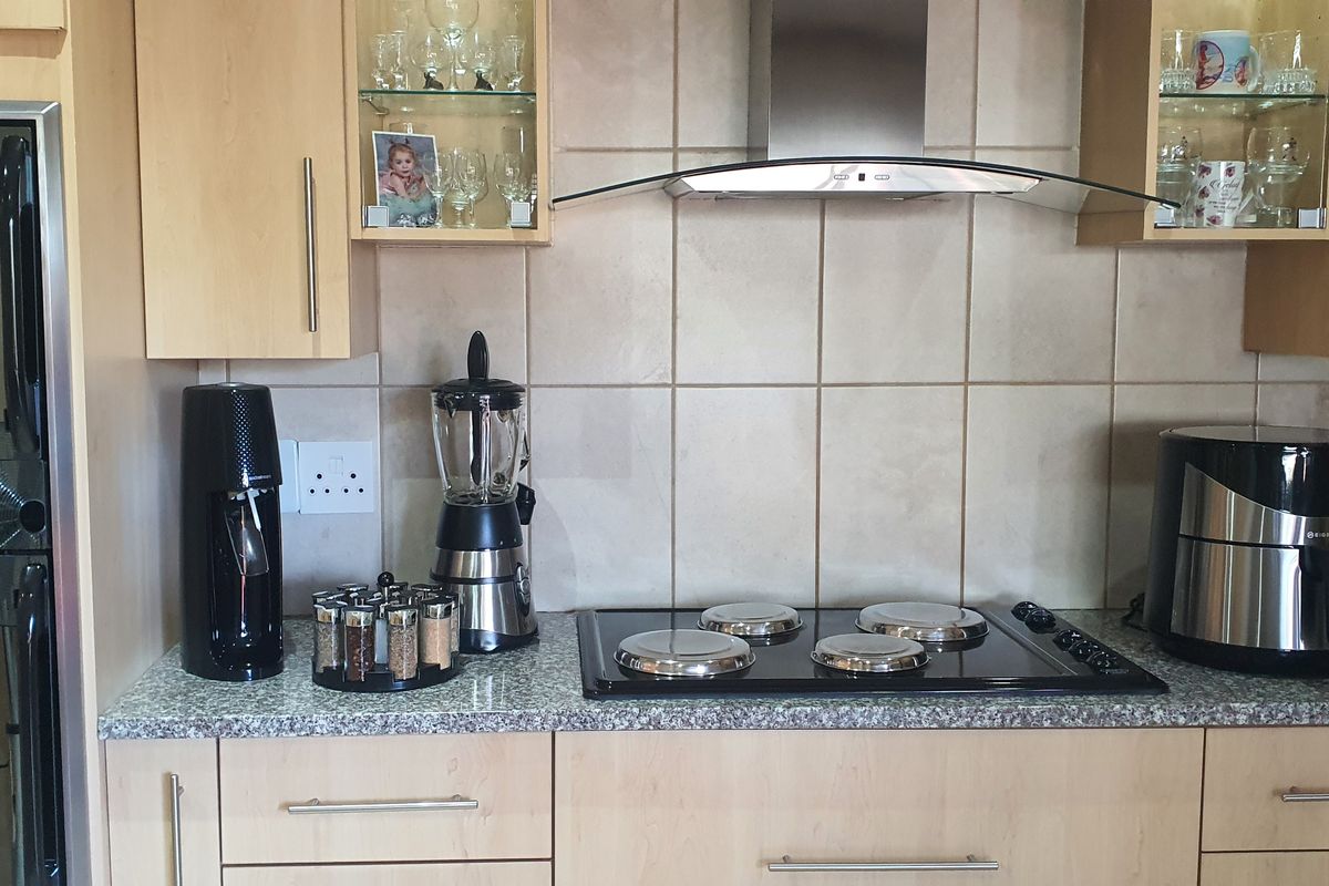 A functional kitchen area featuring light wood cabinetry, granite countertops, a tiled backsplash, and a built-in electric hob with a stainless steel extractor fan.