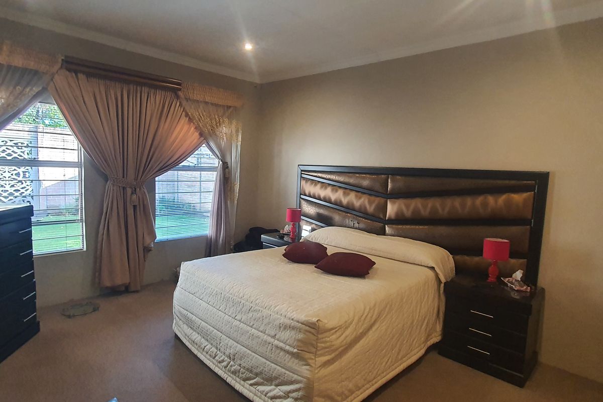 A spacious bedroom featuring neutral wall tones, carpeted flooring, and large windows with integrated security bars, providing a comfortable and functional living space.