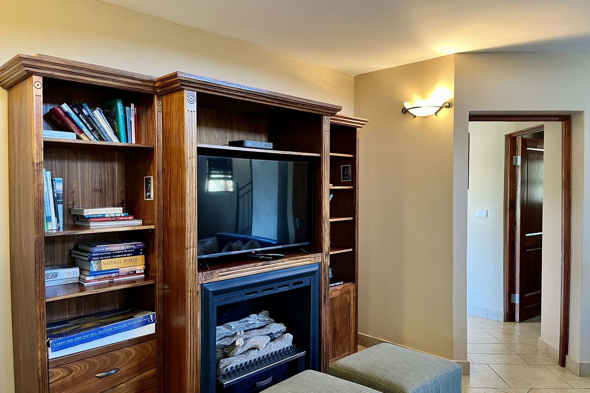 A cozy living area featuring a built-in wooden entertainment unit with an integrated fireplace and shelving, leading into a tiled hallway.