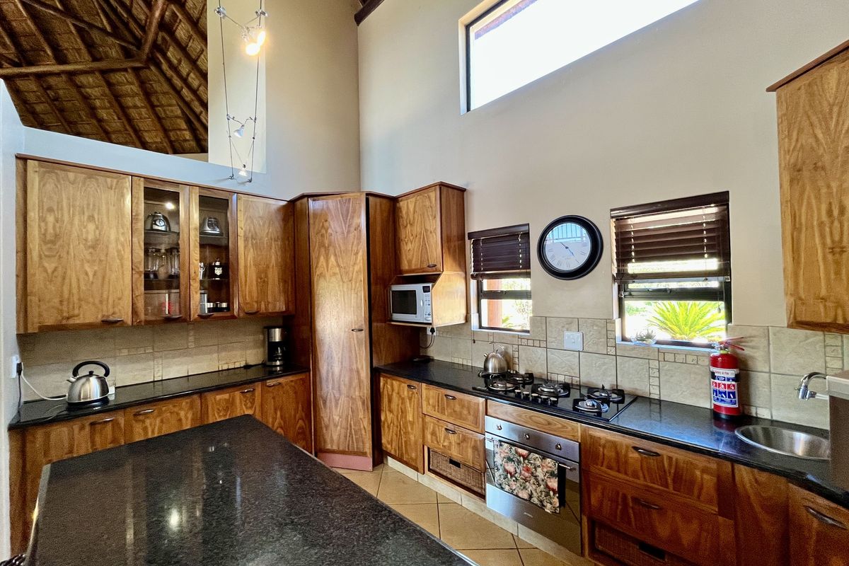 A spacious kitchen featuring wooden cabinetry, granite countertops, a built-in gas hob, oven, and high vaulted ceilings with exposed thatch detailing.