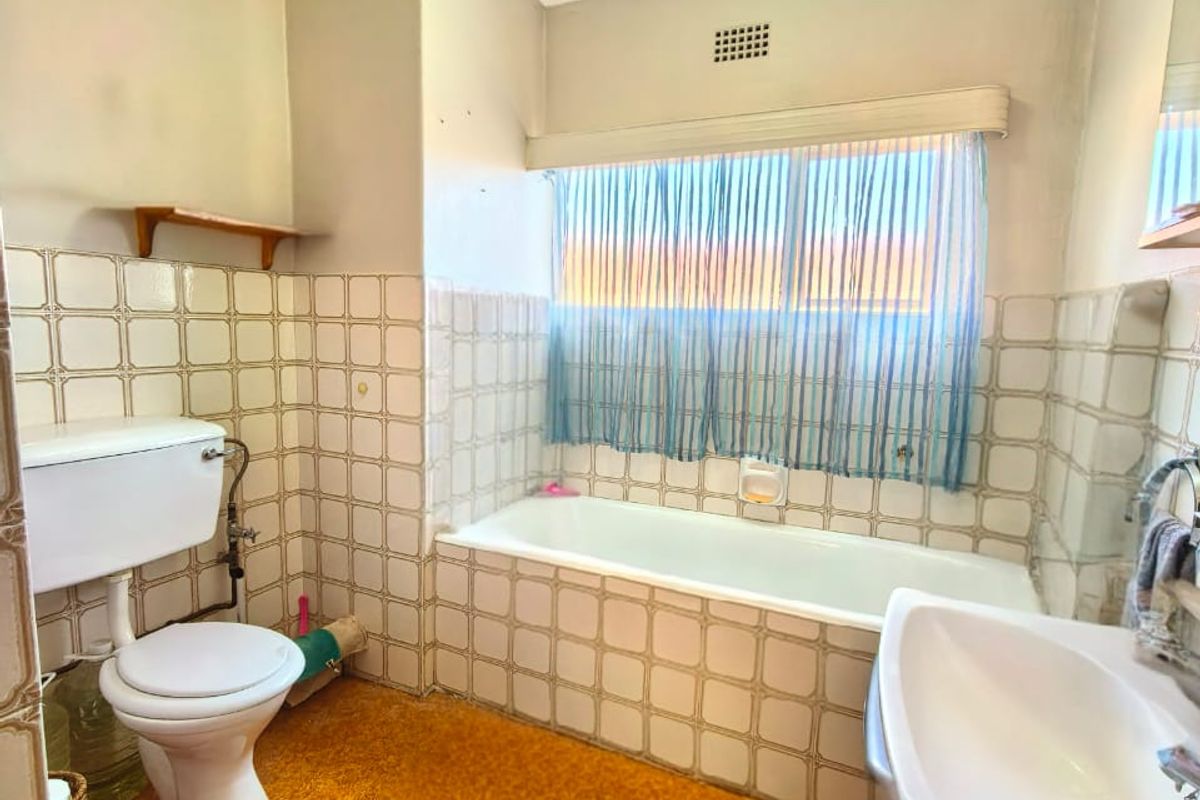 A dated bathroom featuring a standard bathtub, pedestal basin, and toilet, finished with original wall tiles and textured flooring.
