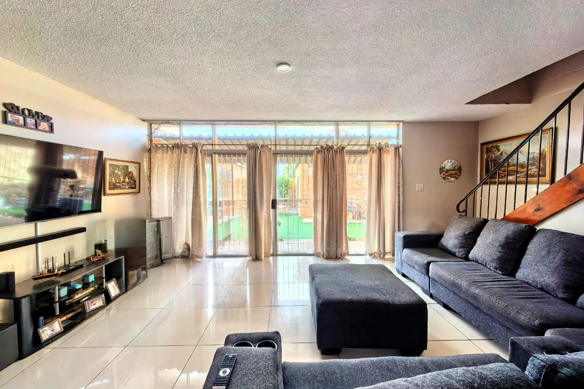 Spacious living room featuring large sliding glass doors leading to the patio, tiled flooring, and an integrated staircase.