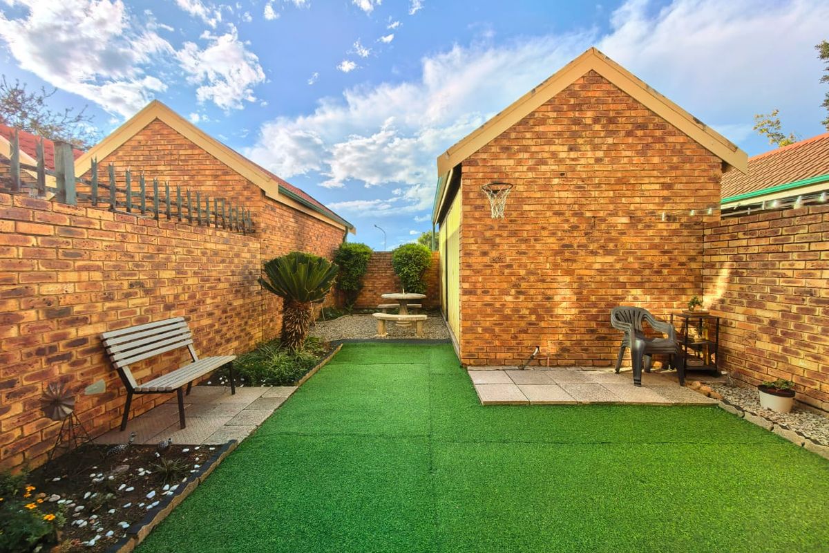 A private rear courtyard featuring a low-maintenance artificial lawn, brick boundary walls, and paved seating areas between two brick structures.