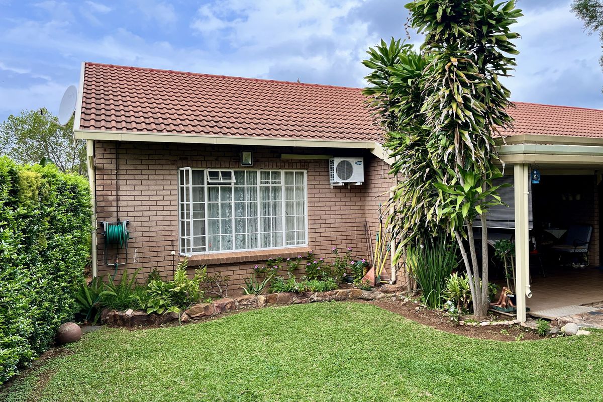 A well-maintained rear exterior view of the townhouse featuring a brick facade, tiled roof, air conditioning unit, and a landscaped garden area.