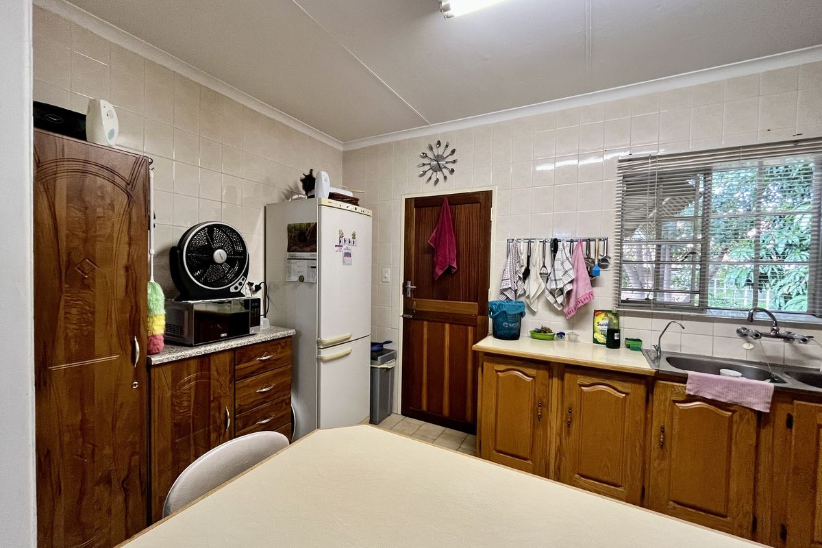 A functional kitchen featuring wooden cabinetry, tiled walls, a double basin sink, and a window with security bars.