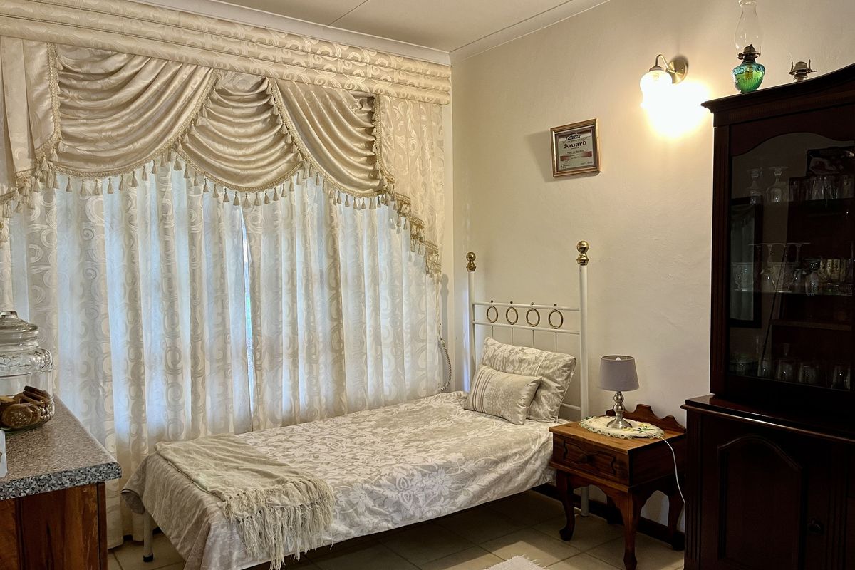 A bedroom featuring tiled flooring, neutral walls, and a window with decorative pelmet and curtain treatments.