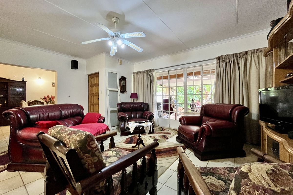 A spacious living room featuring tiled flooring, a ceiling fan, and large glass sliding doors providing access to the outdoor patio area.