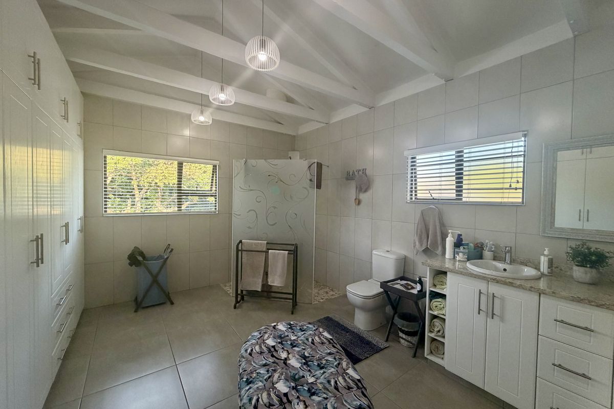 Spacious bathroom featuring vaulted ceilings with exposed beams, a large walk-in shower, built-in cabinetry, and a vanity with a stone countertop.