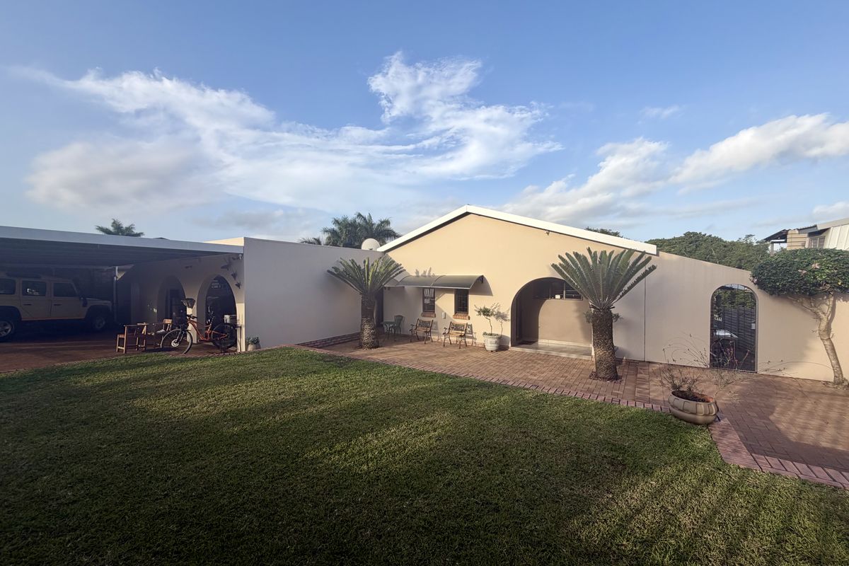 A well-maintained rear exterior view featuring a paved patio area, a manicured lawn, and a covered carport structure with arched architectural details.