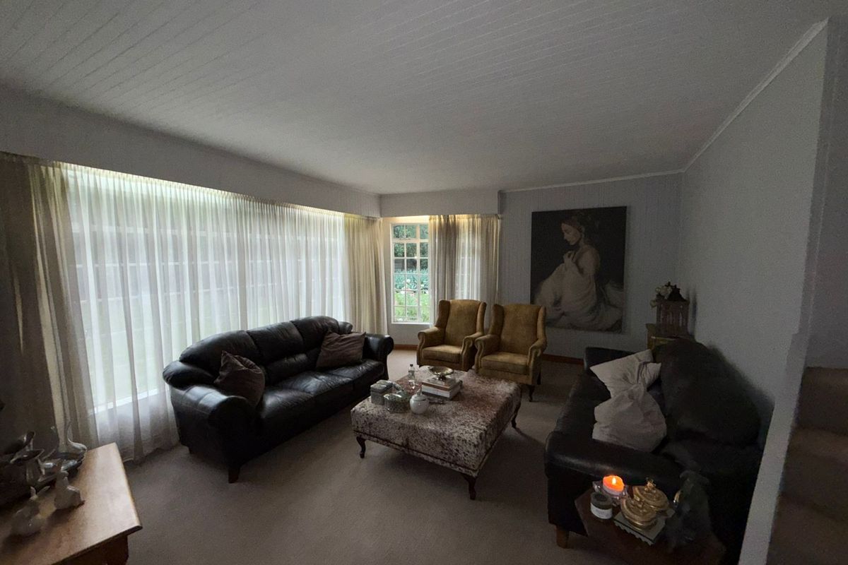 A spacious living room featuring large windows with floor-to-ceiling curtains, providing ample natural light and a view of the garden.