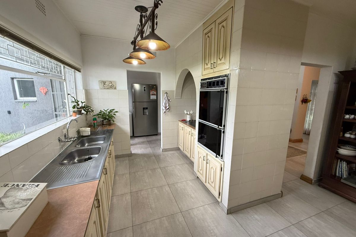A functional kitchen featuring tiled flooring, built-in cabinetry, a double sink, and a built-in double oven, with an arched transition to the adjacent space.