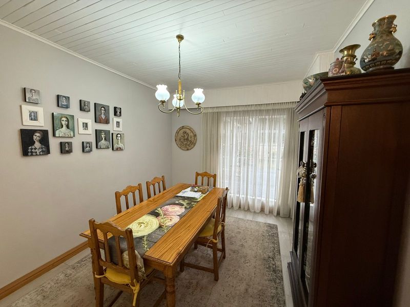 A traditional dining room featuring a white tongue-and-groove ceiling, tiled flooring, and a large window with sheer curtains providing natural light.