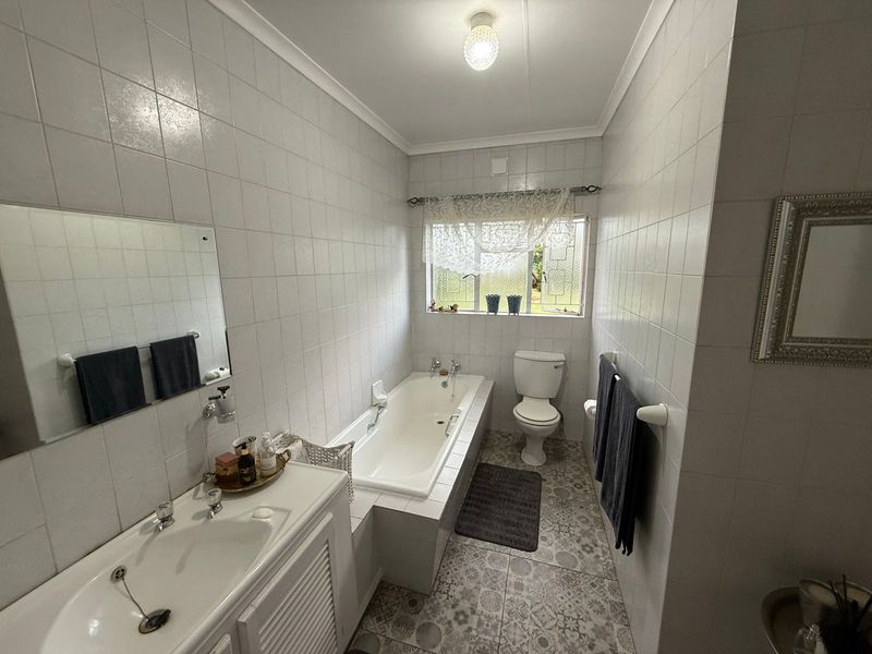 A functional bathroom featuring a built-in bathtub, a vanity basin, and a toilet, finished with classic wall tiles and patterned floor tiles.