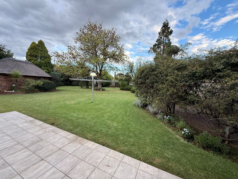 A spacious, well-maintained rear garden featuring a tiled patio area, established trees, and a lush green lawn.
