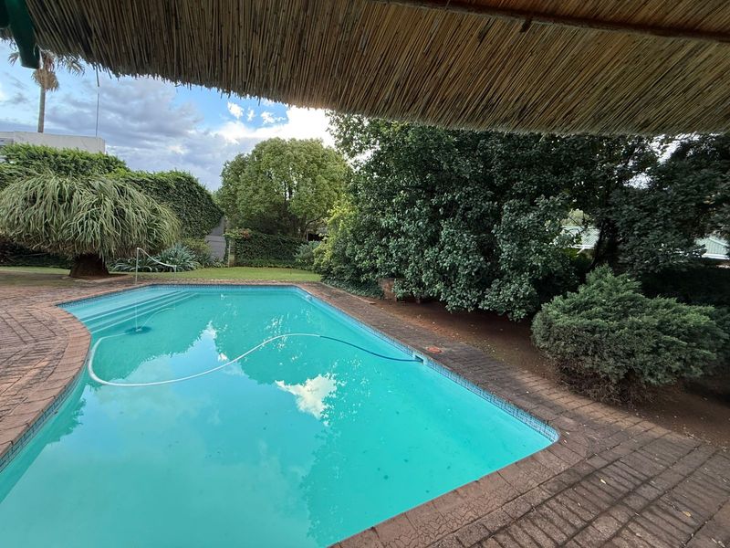 A private swimming pool area featuring brick paving, mature garden landscaping, and a thatched outdoor cover, ideal for relaxation and outdoor entertainment.