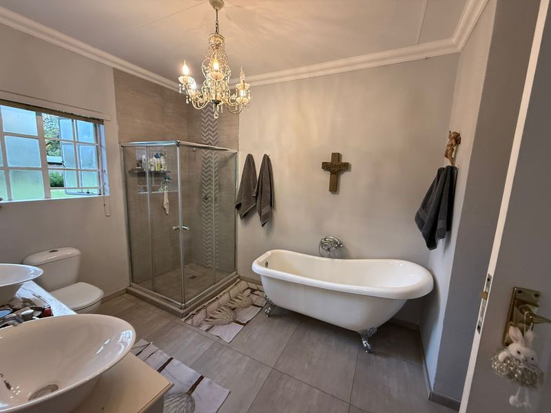A well-appointed bathroom featuring a classic clawfoot bathtub, a separate glass-enclosed shower, dual vessel sinks, and elegant chandelier lighting.