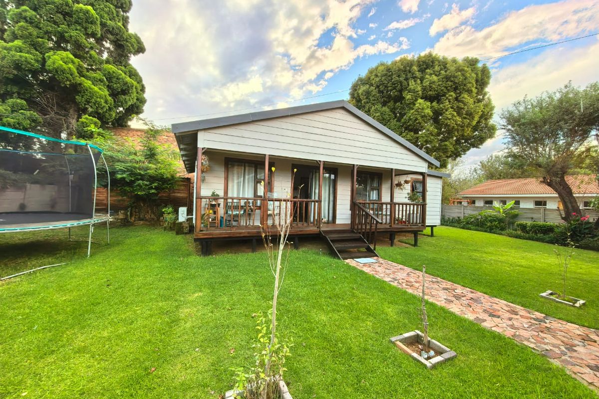 A charming detached cottage featuring a raised timber deck, wooden balustrades, and a stone pathway set within a spacious, well-maintained garden.