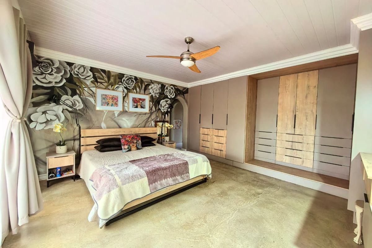 Spacious bedroom featuring a large built-in wardrobe with wood-tone accents, a ceiling fan, and a decorative floral feature wall.