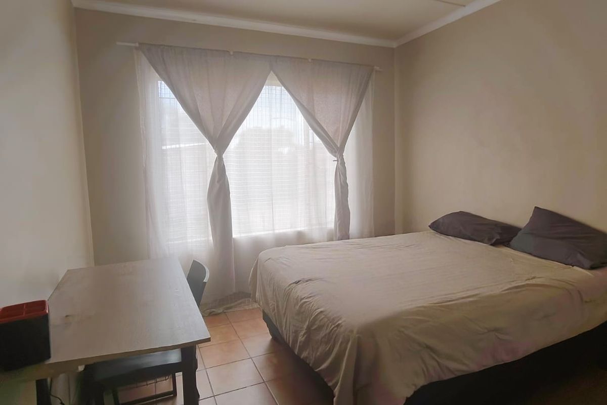 A functional bedroom featuring tiled flooring and a large window, providing a simple and practical living space.