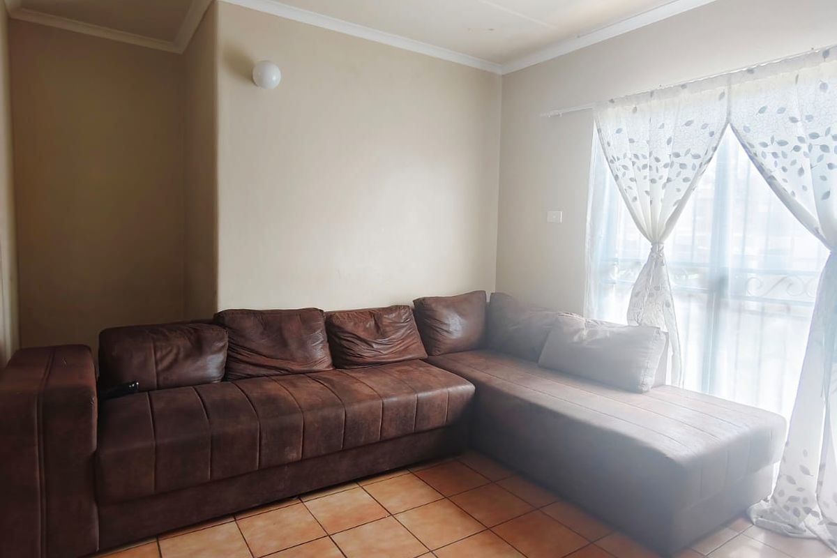 A living room featuring ceramic floor tiles, neutral wall paint, and a large window with curtain fixtures.
