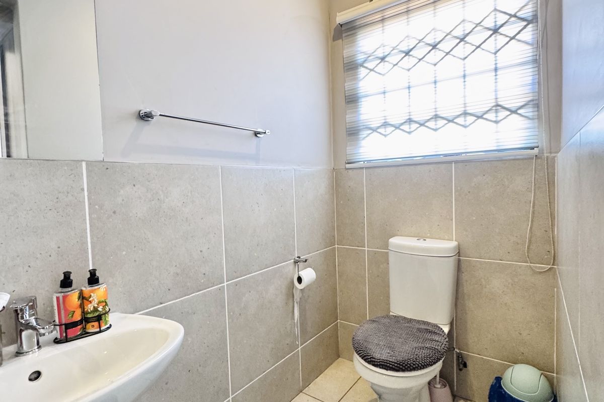 A functional guest bathroom featuring a pedestal basin, a standard toilet, and neutral wall and floor tiling.