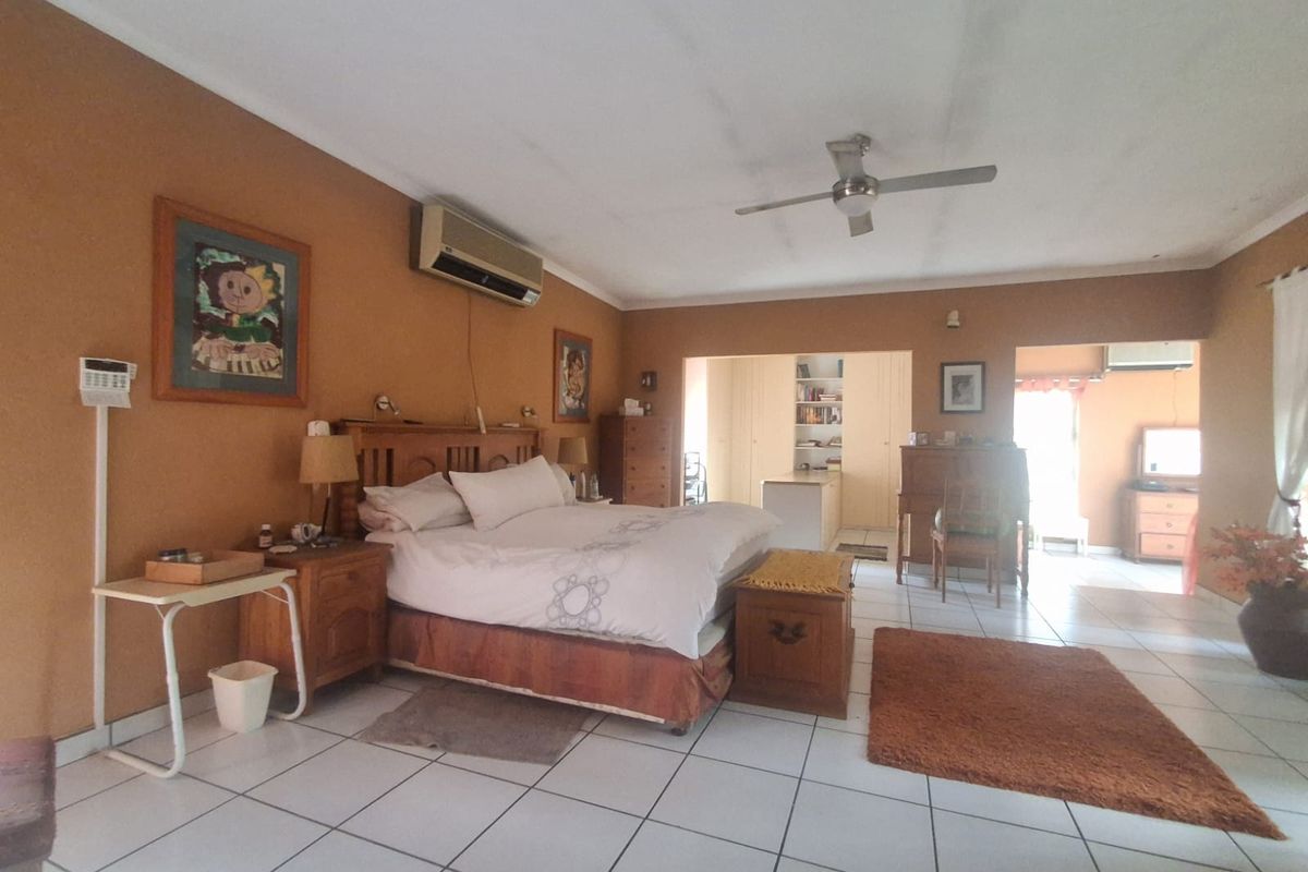 Spacious bedroom featuring tiled flooring, a ceiling fan, and a wall-mounted air conditioning unit, with an adjoining walk-in closet or dressing area.