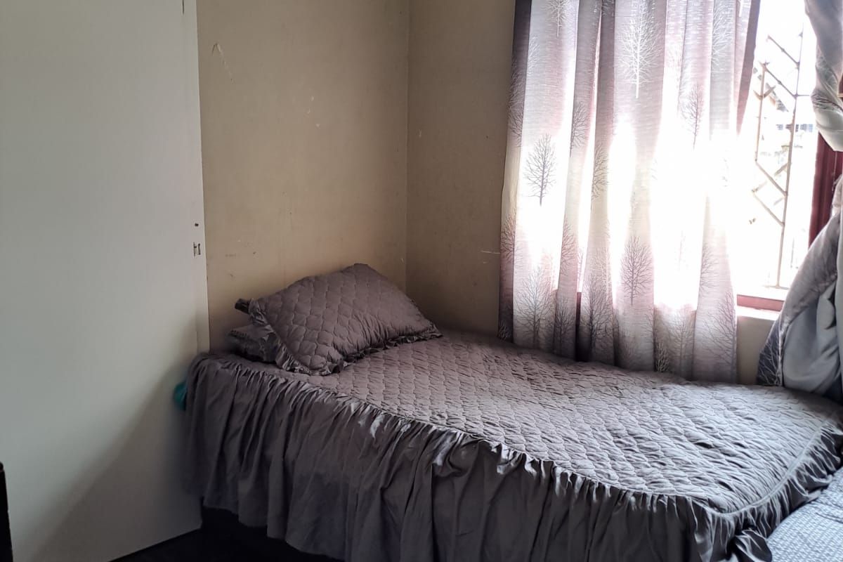 A compact bedroom featuring dark floor tiles, a window with fitted curtains, and a standard interior door.