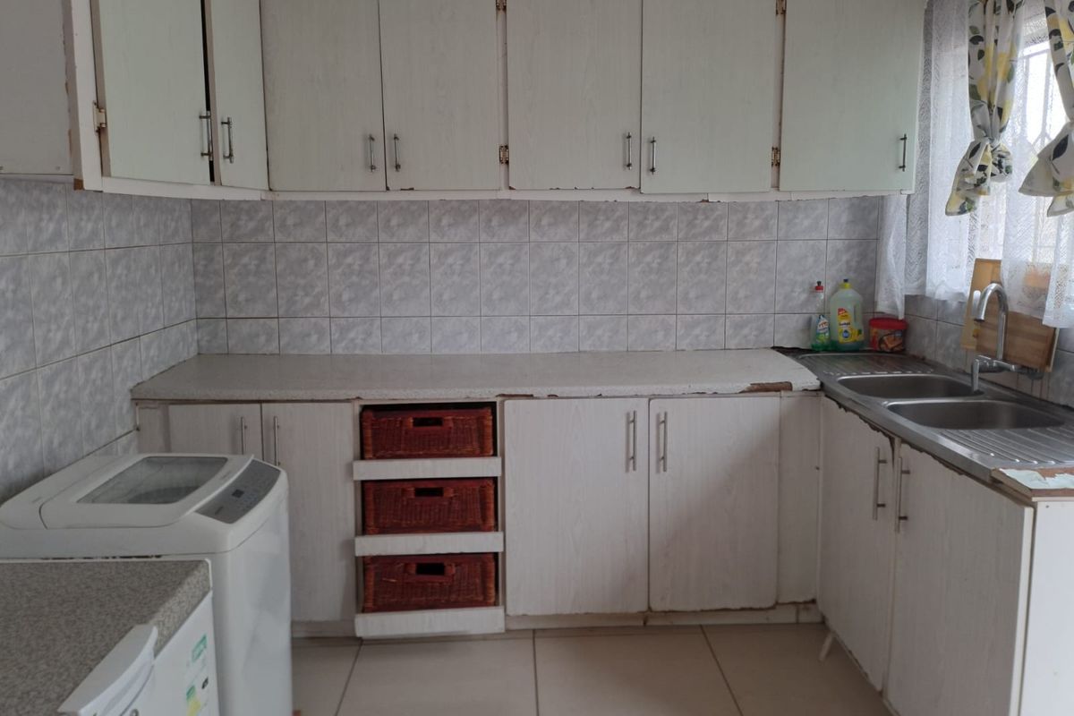 A functional kitchen featuring white cabinetry, tiled splashbacks, a double stainless steel sink, and tiled flooring with space for laundry appliances.