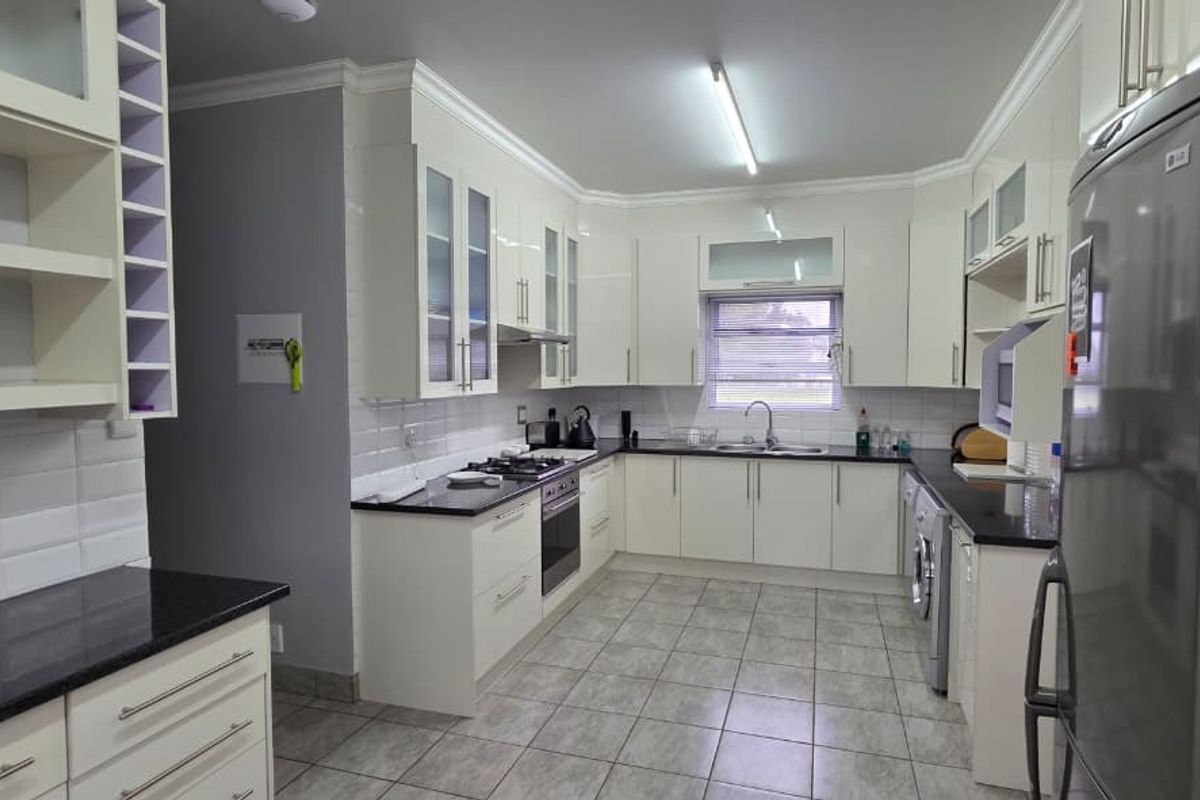 Modern kitchen featuring white high-gloss cabinetry, dark granite countertops, tiled backsplash, and integrated stainless steel oven and hob.