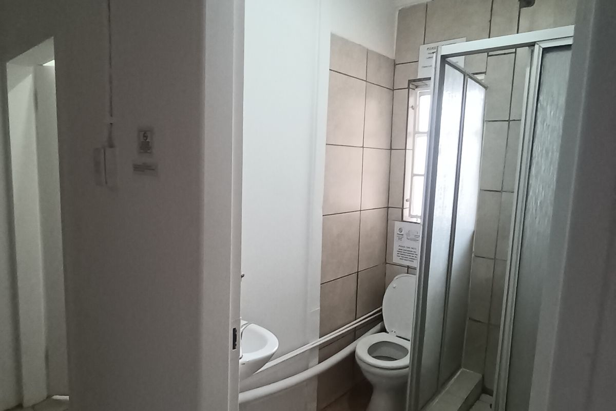 A compact bathroom featuring a shower enclosure, toilet, and wall-mounted basin with visible surface-mounted plumbing.