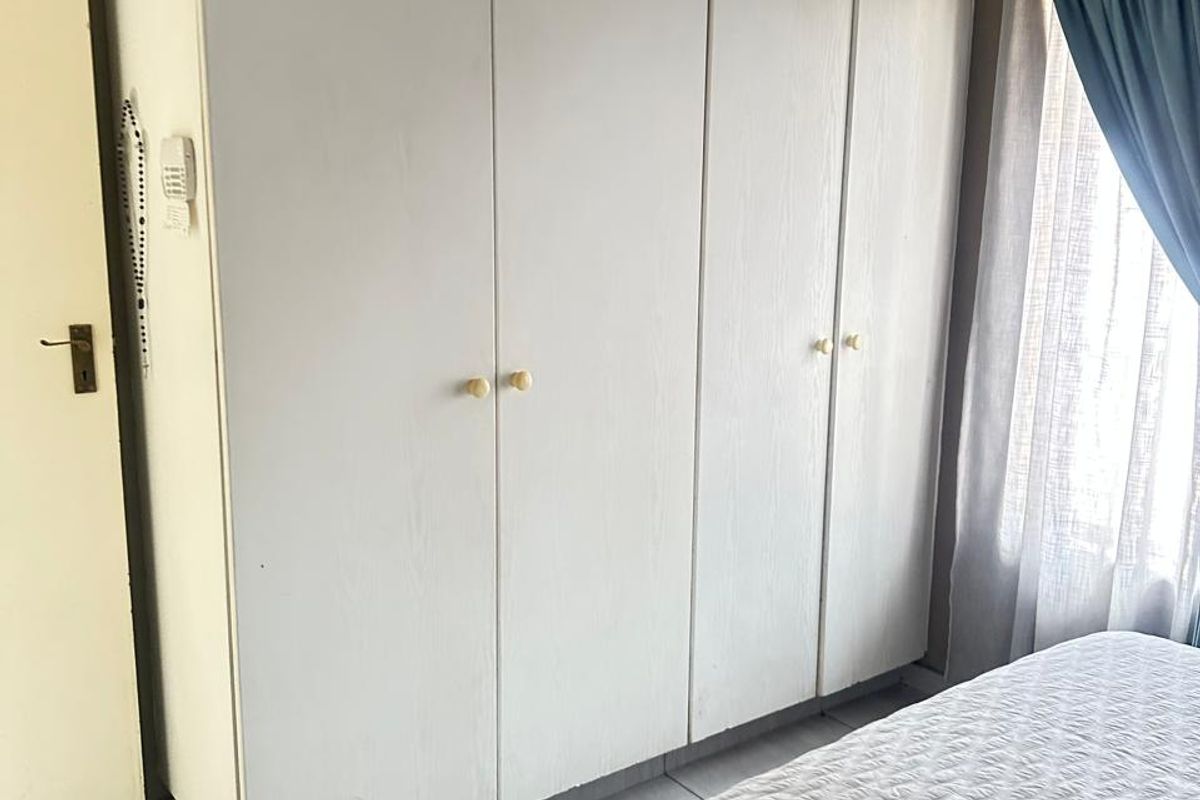 A bedroom featuring built-in white cabinetry with simple hardware, tiled flooring, and a window with curtain treatments.