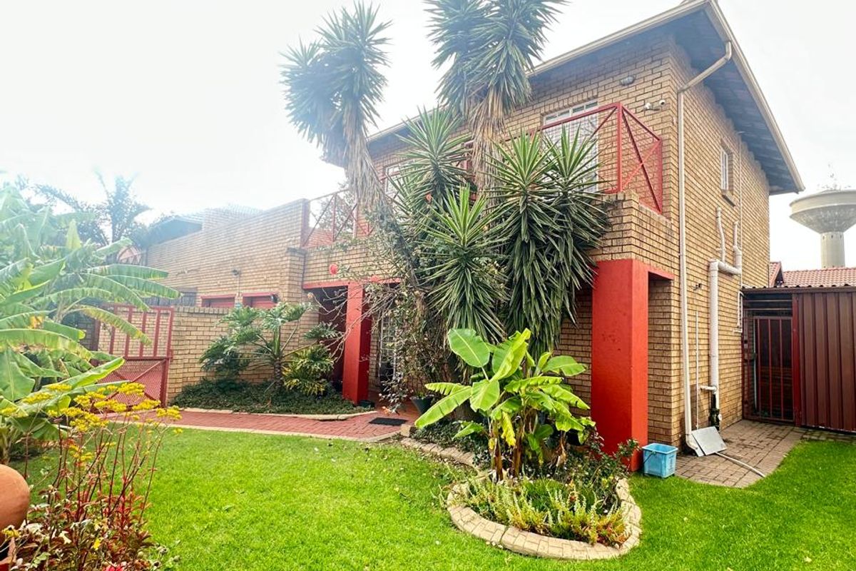 Rear view of a townhouse featuring a brick facade, upper-level balcony with metal railing, and a landscaped garden with paved pathways.