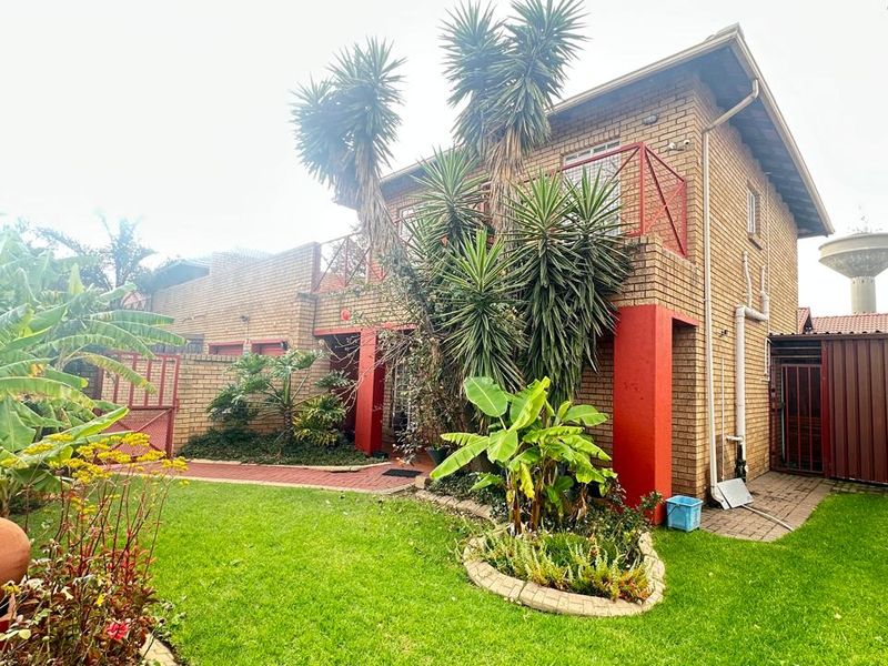Rear view of a townhouse featuring a brick facade, upper-level balcony with metal railing, and a landscaped garden with paved pathways.