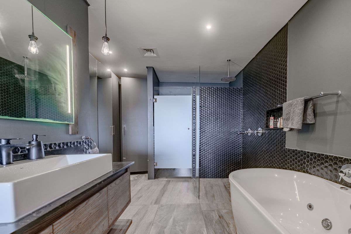 Modern bathroom featuring a freestanding soaking tub, walk-in glass shower, floating vanity with vessel sink, and stylish dark hexagonal wall tiling.