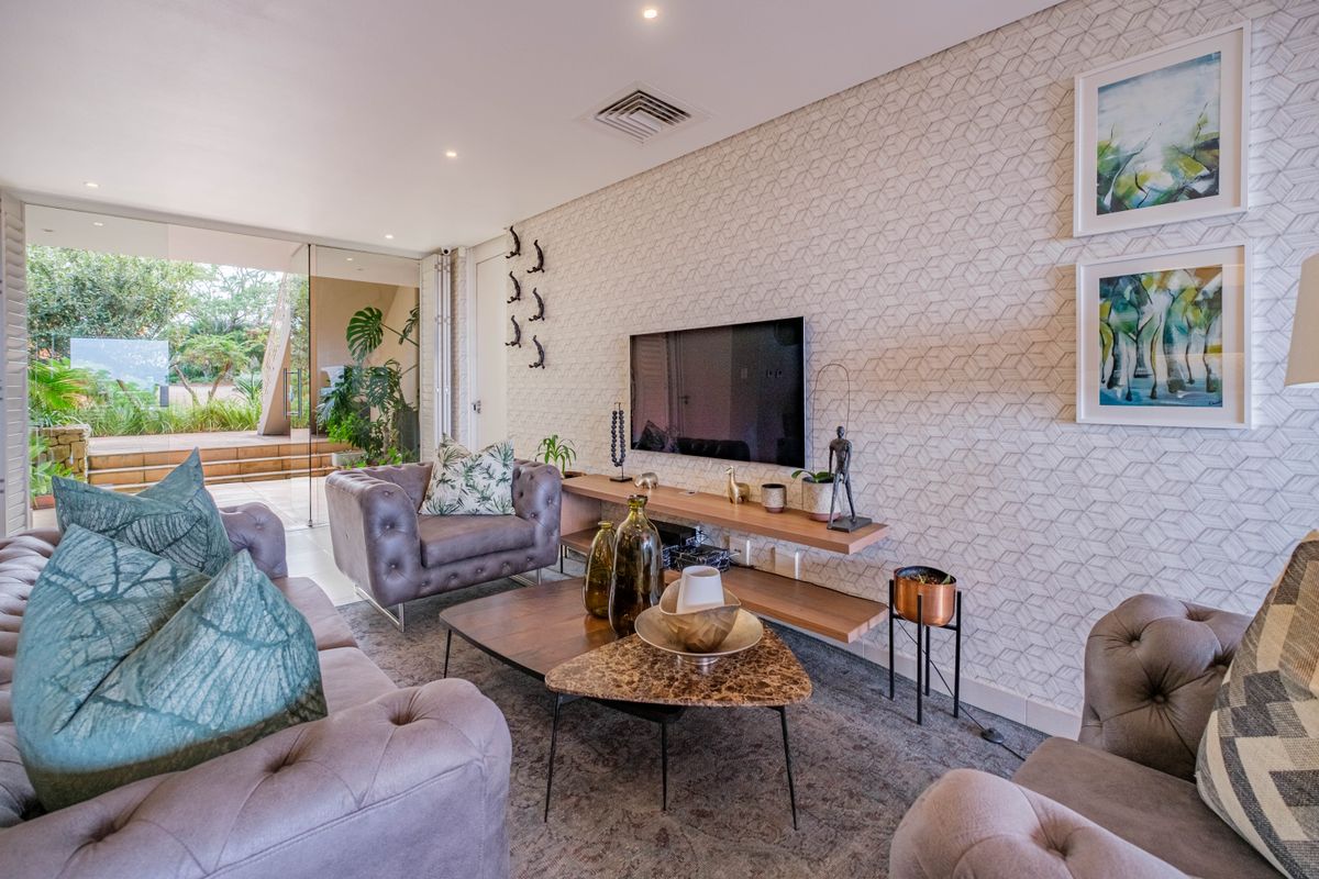 A well-appointed living room featuring textured wallpaper, recessed ceiling lighting, and seamless glass sliding doors opening onto a private patio area.