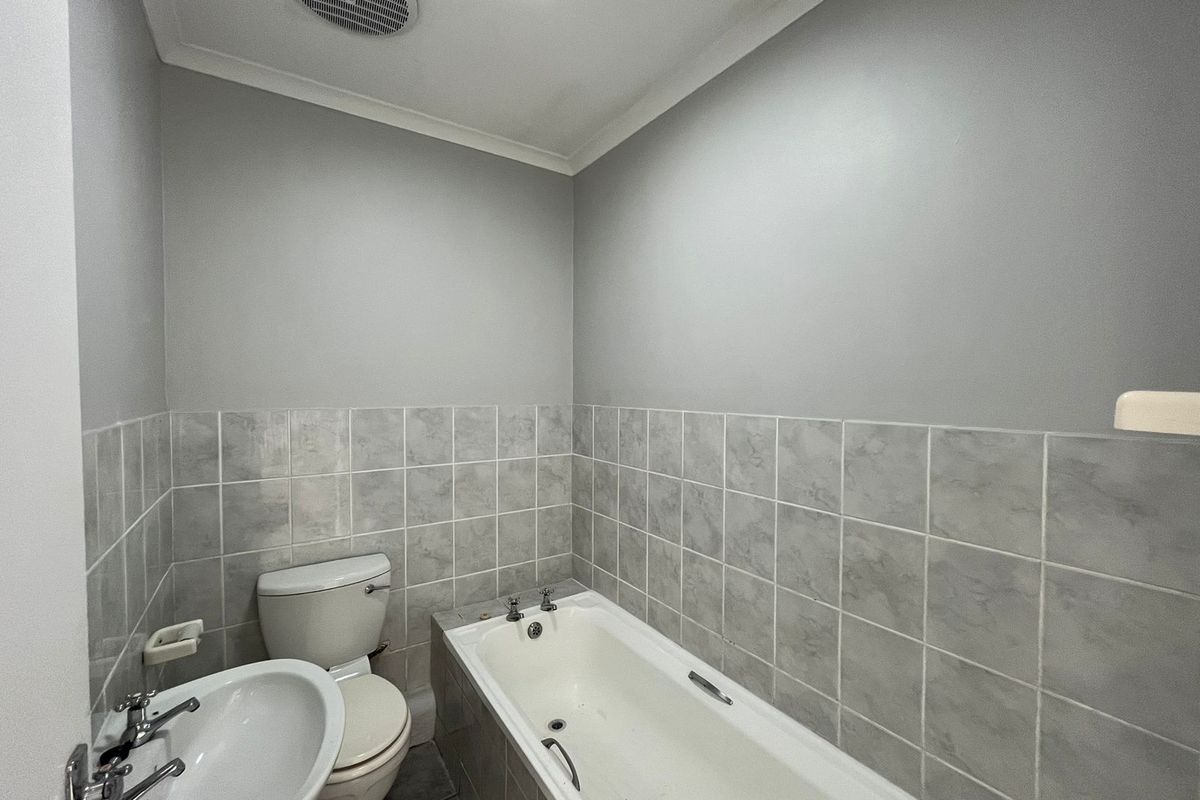 A functional bathroom featuring a bathtub, pedestal basin, and toilet with neutral grey wall paint and tiled splashbacks.