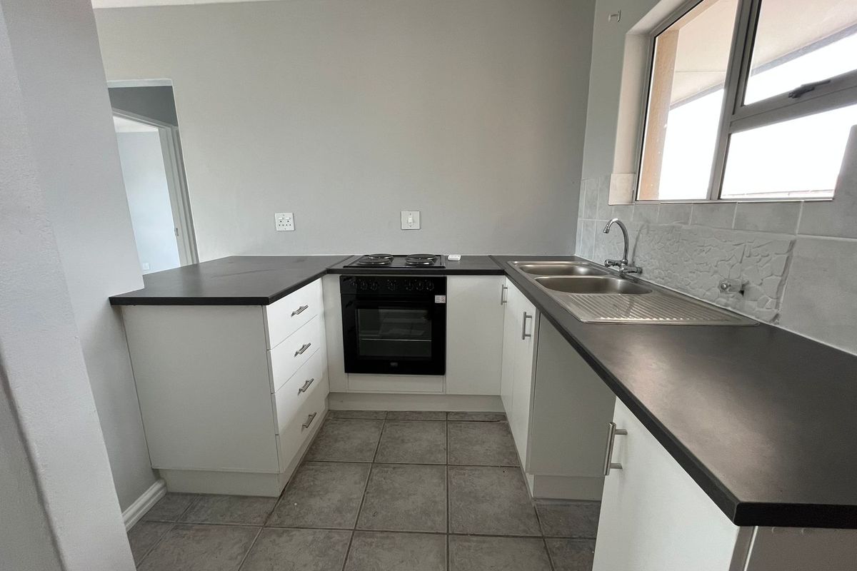 A clean, functional kitchen featuring white cabinetry, dark laminate countertops, a built-in oven with hob, and a double sink with tiled backsplash.