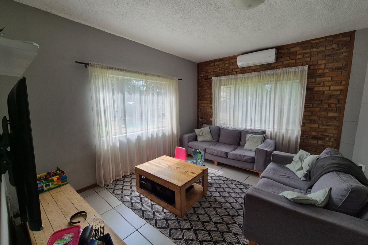 A comfortable living room featuring a rustic exposed brick feature wall, tiled flooring, and a wall-mounted air conditioning unit.